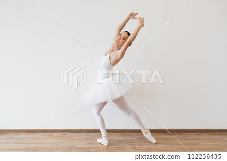 Caucasian woman ballerina in white tutu, dancing on pointe with arms overhead. 112236435