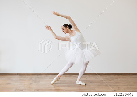 Caucasian woman ballerina in white tutu, dancing on pointe with arms overhead. Caucasian woman ballerina in white tutu, dancing on pointe with arms overhead. 112236445