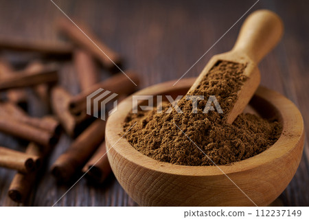 Close-up cinnamon powder in a wooden bowl on a dark wooden table. 112237149