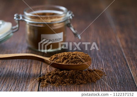 cinnamon powder poured out of a wooden spoon on a dark wooden table, selective focus. 112237152