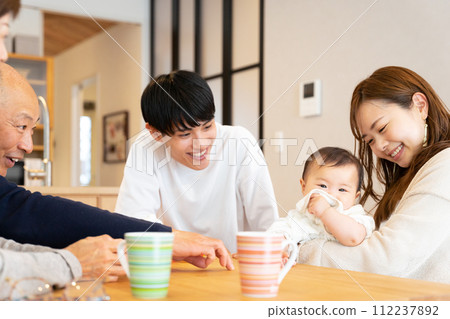 一家三口:父親、母親和祖父母在客廳抱著一個嬰兒。 一家三口:父親、母親和祖父母在客廳抱著一個嬰兒。 112237892
