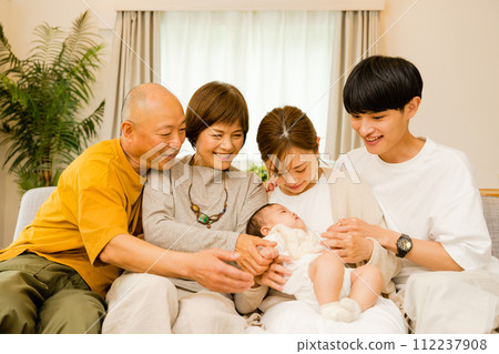 一大家人的年長祖父母和父母坐在沙發上，看著母親抱著的0歲嬰兒。 112237908
