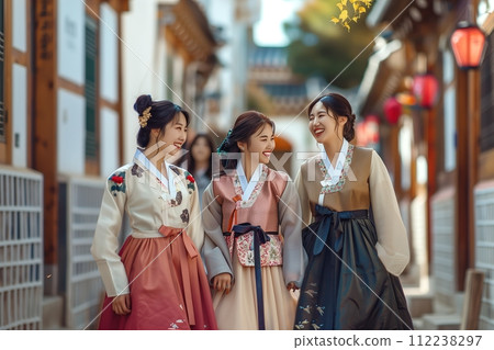 Three women in traditional Korean clothing are walking down a street, smiling 112238297