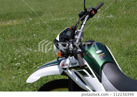 Parked off-road bike 2 receiving strong sunlight from above in a sunny midday spring meadow Parked off-road bike 2 receiving strong sunlight from above in a sunny midday spring meadow 112238399