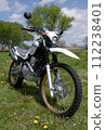 A parked off-road motorcycle receiving strong sunlight from above in a sunny midday spring meadow 1 112238401