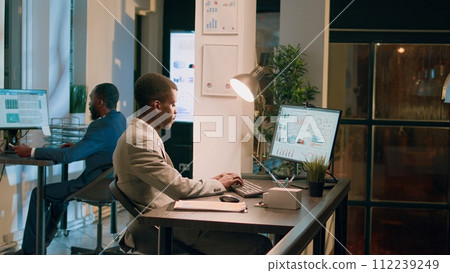 Employees working together overnight on finishing project before impending next day deadline. Hardworking office staff members solving various company project tasks during nightshift Employees working together overnight on finishing project before impending next day deadline. Hardworking office staff members solving various company project tasks during nightshift 112239249