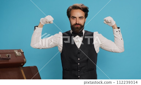 Strong employee flexing arm muscles in studio, indicating power and strength underneath his classy suit and tie. Hotel porter doorman feeling powerful on camera, tourism sector concept. Strong employee flexing arm muscles in studio, indicating power and strength underneath his classy suit and tie. Hotel porter doorman feeling powerful on camera, tourism sector concept. 112239314