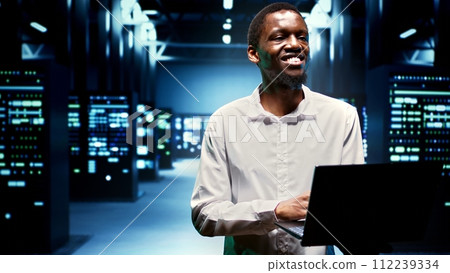 Happy engineer walking between supercomputers in high performance computing server room, ensuring flawless operations conditions. Professional monitoring data center hardware energy consumption 112239334