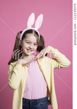 Cute schoolgirl with pigtails and bunny ears fooling around in the studio, playing and doing dance moves. Positive cheerful kid feeling confident and excited about easter, beautiful toddler. 112239379
