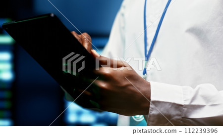 IT programmer using tablet to monitor supercomputer hub security features protecting against unauthorized access, data breaches, phishing attacks and other cybersecurity dangers, close up IT programmer using tablet to monitor supercomputer hub security features protecting against unauthorized access, data breaches, phishing attacks and other cybersecurity dangers, close up 112239396