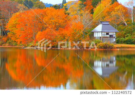 A hut on the lake reflecting the autumn leaves 112240572