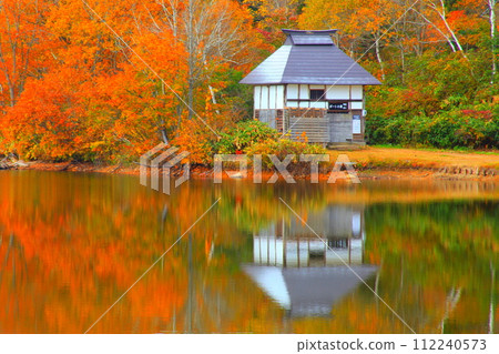 A hut on the lake reflecting the autumn leaves 112240573