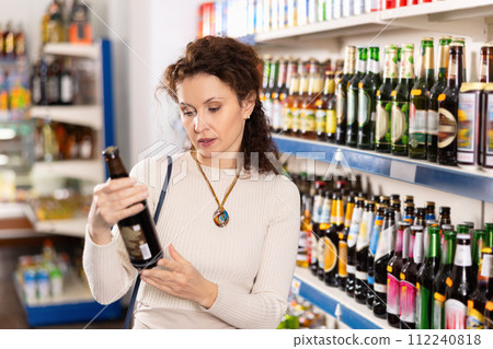 In Russian goods store, woman choose bottle of beer 112240818