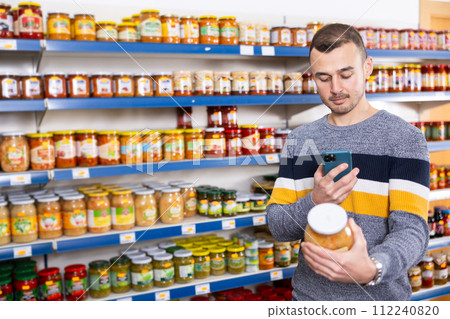 In Russian goods store, man choose jar of pickled fermented cabbage and photographs label In Russian goods store, man choose jar of pickled fermented cabbage and photographs label 112240820