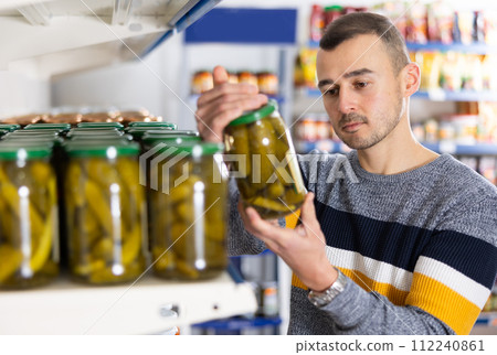 Attentive man buying canned cucumbers at grocery store 112240861