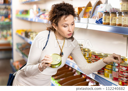 Adult woman chooses sprats in store 112240882