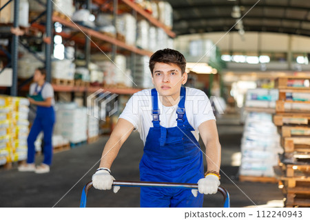 Young loader guy pushing cart in warehouse Young loader guy pushing cart in warehouse 112240943