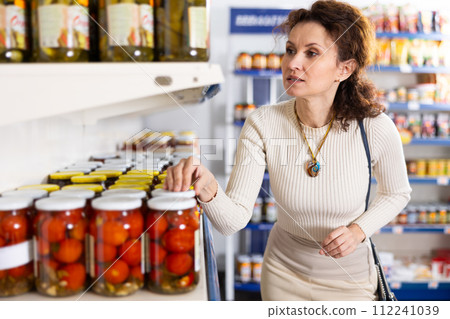 In Russian goods store, woman choose jar of pickled tomatoes In Russian goods store, woman choose jar of pickled tomatoes 112241039