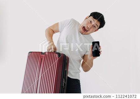 Asian man carrying a suitcase and holding mobile phone, showing application for travel and booking. 112241072