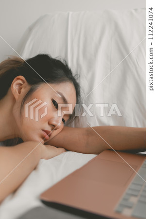 Asian Thai woman fall asleep, sleeping and resting head on her arm while working and using laptop on white couch, relaxing at room apartment. Asian Thai woman fall asleep, sleeping and resting head on her arm while working and using laptop on white couch, relaxing at room apartment. 112241074