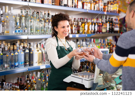 Adult saleswoman selling sausages to man 112241123