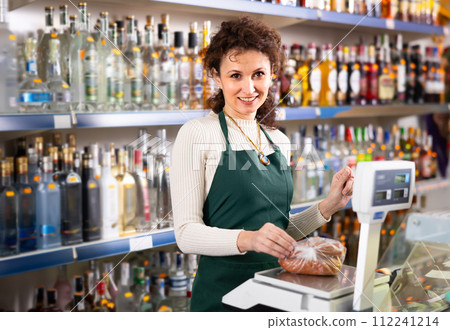 Woman grocery store clerk weighs sausages on scale Woman grocery store clerk weighs sausages on scale 112241214