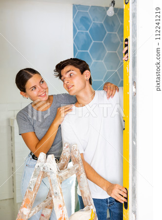 Interested couple inspecting evenness of wall with level meter in house under construction 112241219