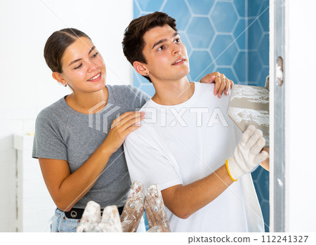 Couple in the bathroom glues ceramic tiles on the wall 112241327