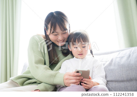 父母和孩子（母親和女兒）開心地看著智慧型手機的圖片。一起觀看應用程式、影片和遊戲 112241358