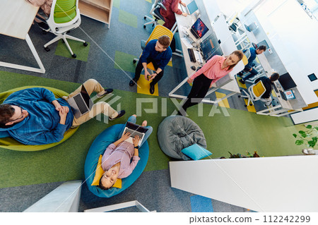 In a modern startup office, a diverse group of young and capable businesspeople engage in lively discussions about various projects, showcasing teamwork, innovation, and entrepreneurial spirit 112242299