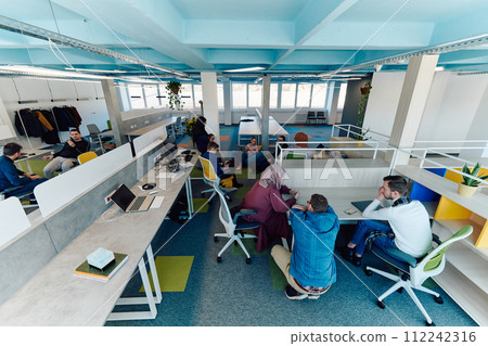 In a modern startup office, a diverse group of young and capable businesspeople engage in lively discussions about various projects, showcasing teamwork, innovation, and entrepreneurial spirit 112242316
