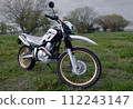 A parked off-road bike 1b reflecting the light from the clouds that has become brighter through the setting sun in a spring evening meadow 112243147