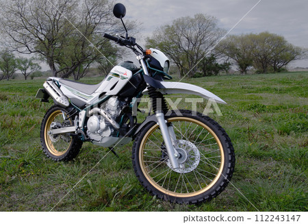 A parked off-road bike 1b reflecting the light from the clouds that has become brighter through the setting sun in a spring evening meadow A parked off-road bike 1b reflecting the light from the clouds that has become brighter through the setting sun in a spring evening meadow 112243147