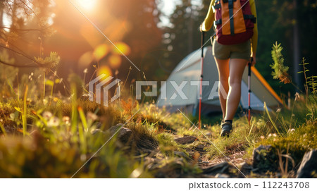 The warm glow of sunrise bathes a campsite as a trekker, equipped with a backpack and hiking poles, embarks on an early morning journey amidst the tranquil beauty of the forest. The warm glow of sunrise bathes a campsite as a trekker, equipped with a backpack and hiking poles, embarks on an early morning journey amidst the tranquil beauty of the forest. 112243708