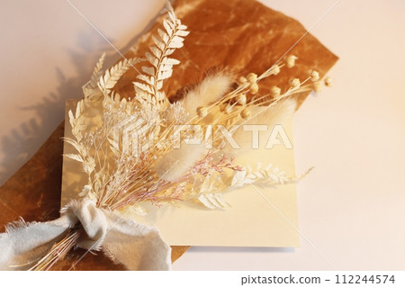 White dried flowers placed on brown waxed paper and a small brown vase, illuminated by the color of a light bulb White dried flowers placed on brown waxed paper and a small brown vase, illuminated by the color of a light bulb 112244574