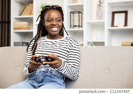 Happy African American Woman Enjoying Gaming on Couch at Home Happy African American Woman Enjoying Gaming on Couch at Home 112247487