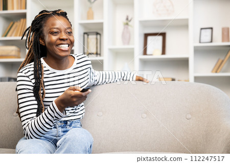 Afro American Woman Enjoying Leisure Time with Remote at Home Afro American Woman Enjoying Leisure Time with Remote at Home 112247517