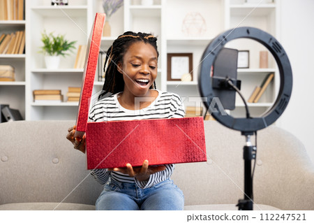 Happy Afro American Woman Unboxing Red Parcel in Living Room 112247521