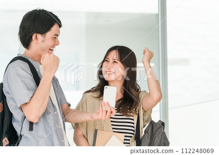 男女學生/大學生一邊看著智慧型手機,一邊高興地揮舞著拳頭 男女學生/大學生一邊看著智慧型手機,一邊高興地揮舞著拳頭 112248069
