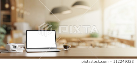 A wooden table features a white-screen laptop computer mockup in a modern Scandinavian coffee shop. 112249328