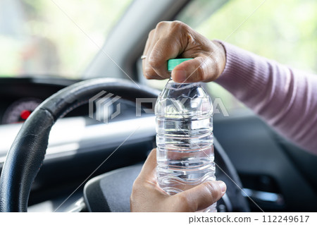 Asian woman driver holding bottle for drink water while driving a car. Plastic hot water bottle cause fire. 112249617