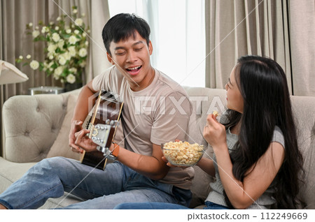 Happy Asian couple enjoying playing guitar and singing at home, having a cute romantic time together Happy Asian couple enjoying playing guitar and singing at home, having a cute romantic time together 112249669
