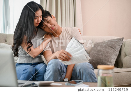 A caring young Asian woman is supporting and encouraging her stressed spouse on the sofa. 112249719