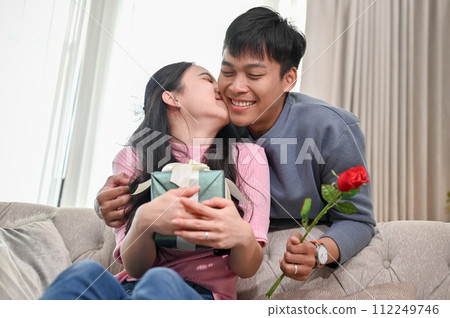A romantic Asian wife is kissing her husband's cheek on a couch to thank him for a special present. A romantic Asian wife is kissing her husband's cheek on a couch to thank him for a special present. 112249746