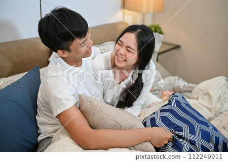 A lovely young Asian couple in pajamas are hugging, playing, and cuddling in bed. 112249911
