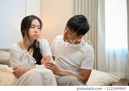 A man apologizes, asking for forgiveness from his sad girlfriend after their argument in the bedroom 112249943