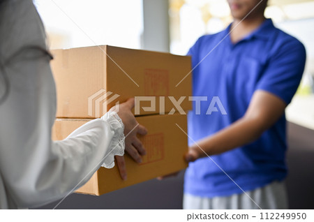 A woman receiving cardboard parcel boxes from a delivery man in front of the house's door. A woman receiving cardboard parcel boxes from a delivery man in front of the house's door. 112249950