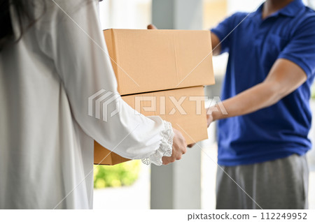 A woman receiving cardboard parcel boxes from a delivery man in front of the house's door. 112249952
