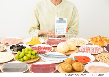 Middle-aged woman with various ingredients and a calculator Middle-aged woman with various ingredients and a calculator 112250040