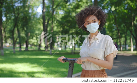 Young woman in protective face mask holding e-scooter, riding in park, rental Young woman in protective face mask holding e-scooter, riding in park, rental 112251749